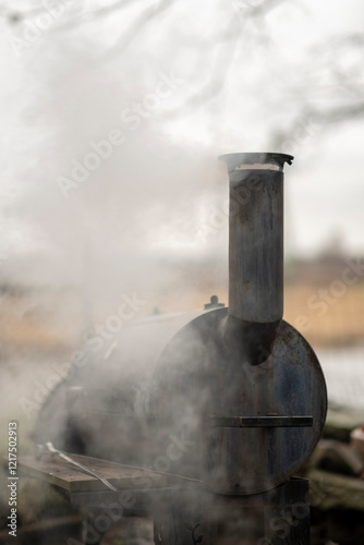 Smoke comes from black offset smoker grill in home backyard, family patio, barbeque party on open air