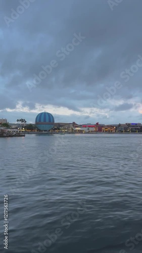 Hot air balloon on the ground at night, filmed from a boat on water with illuminated buildings in the background