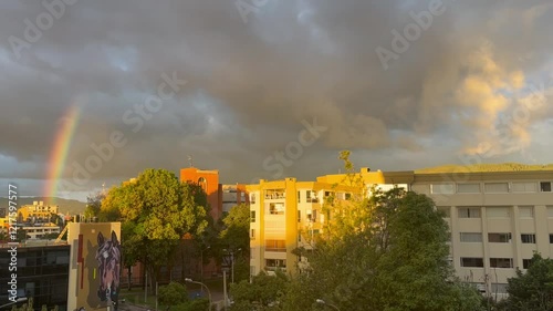  Horizontal panning shot of a city at sunset with a faint rainbow and visible buildings