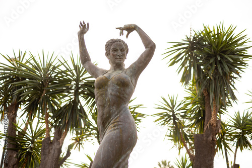 Looking up at statue in honour of Flamenco singer and dancer Lola Flores with palm trees on either side. Actress memorial sculpture