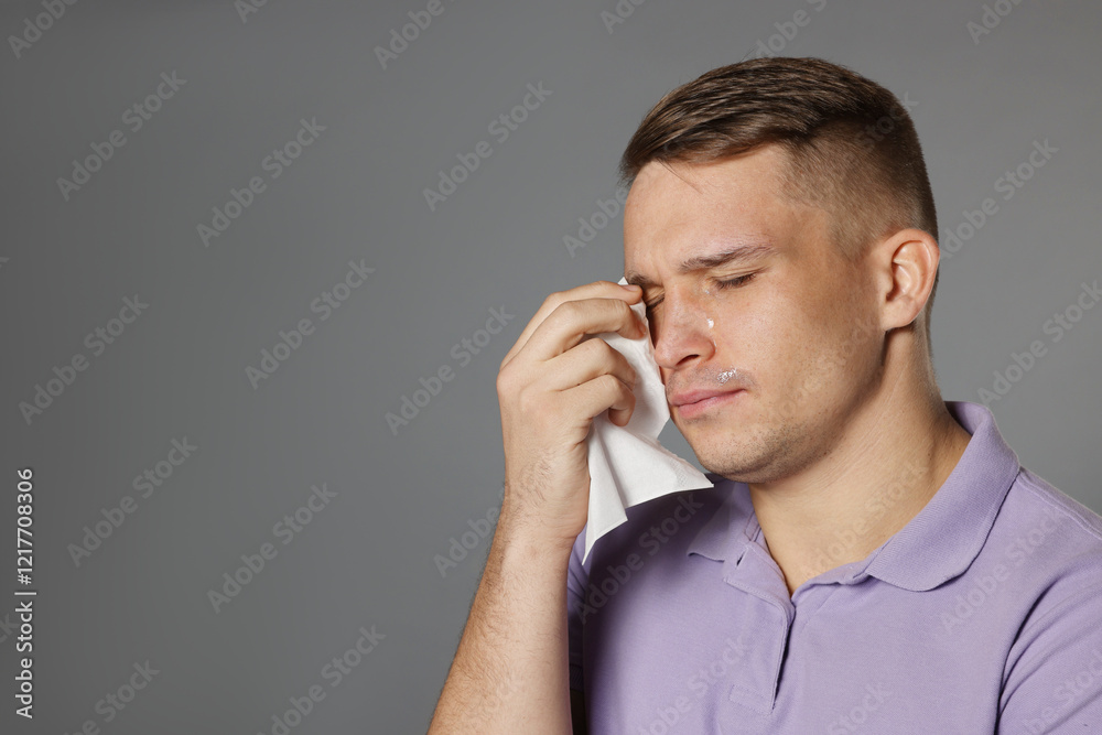 Crying man wiping tears with tissue on grey background. Space for text Crying man wiping tears with tissue on grey background. Space for text