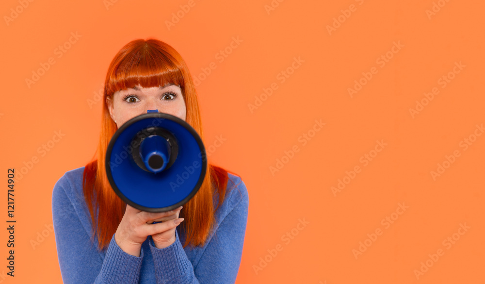 Fototapeta premium A young woman with vibrant red hair holds a blue megaphone while expressing excitement