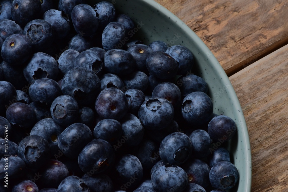 A full bowl of bilberries fragment on a wooden table top view close up macro. A full bowl of bilberries fragment on a wooden table top view close up macro.