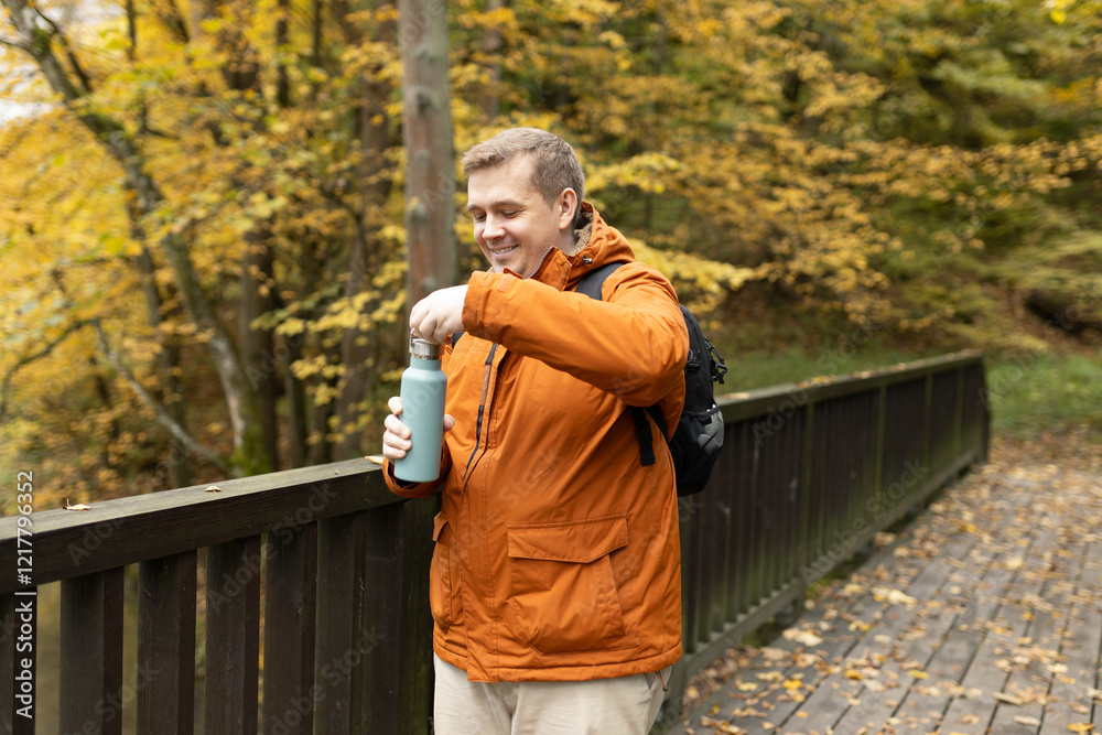 Fototapeta premium 30s Plus size male with backpack smiling outside on an adventure. Hiking, lifestyle, adventure and tourism concept. Young man standing on the bridge in woodland, autumn time.