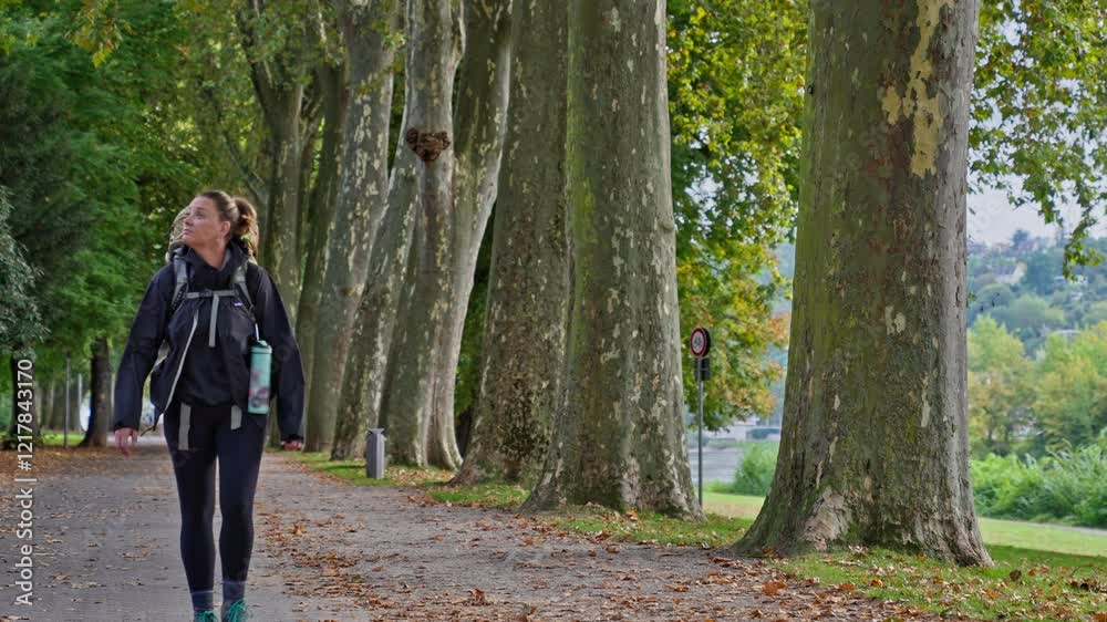 Backpacking woman walking on a tree lined park path in slow motion, Koblenz, Germany Backpacking woman walking on a tree lined park path in slow motion, Koblenz, Germany
