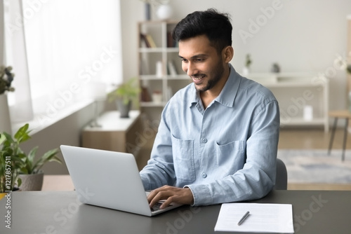 Busy smiling young man type on notebook pc sit at home office desk engaged in accounting work use internet app to get online education manage electronic paperwork check documents make financial report