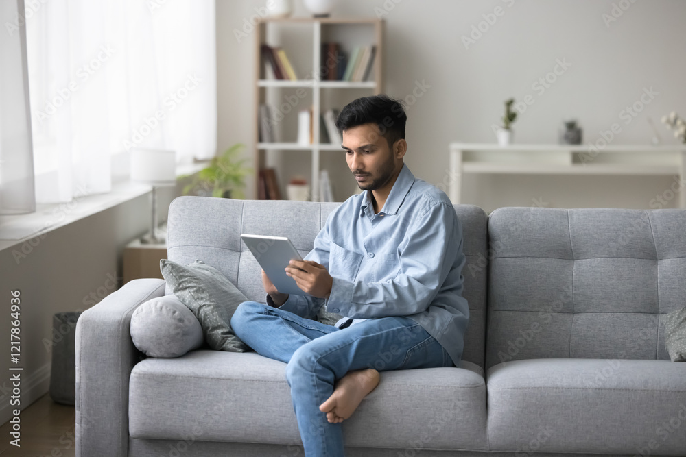 Wireless connection. Young businessman freelance worker sit on sofa engaged in online communication with e-commerce client on tablet pc. Busy male student use e-learning app on pad at home. Copy space Wireless connection. Young businessman freelance worker sit on sofa engaged in online communication with e-commerce client on tablet pc. Busy male student use e-learning app on pad at home. Copy space