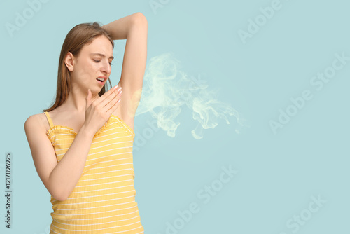 Young woman feeling smell of sweat on blue background. Concept of using deodorant photo