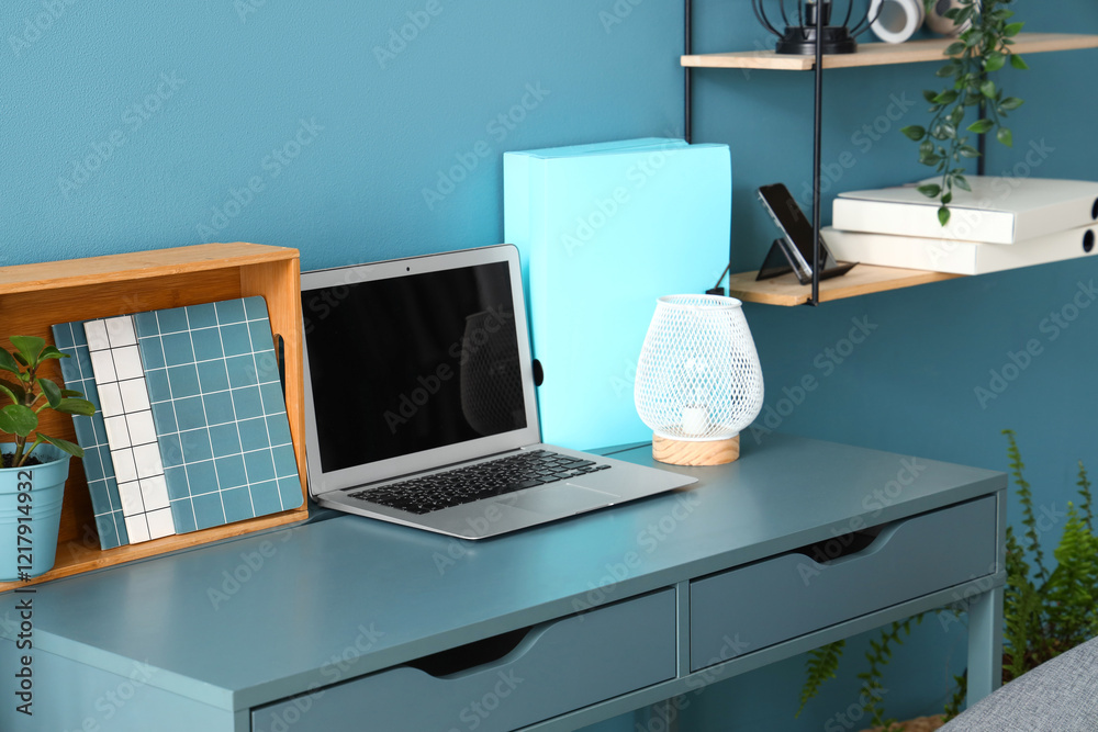 Fototapeta premium Stylish workplace with modern laptop, stationery and lamp near color wall