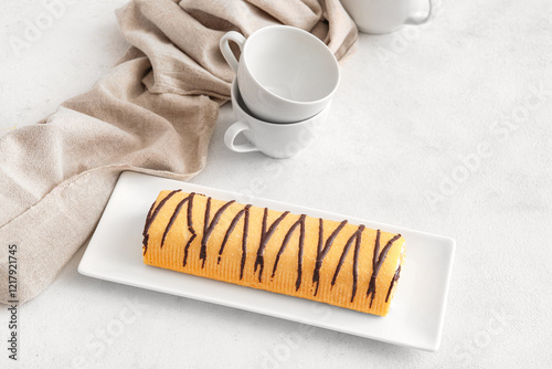 Plate with sweet sponge cake roll and tea cups on white background photo