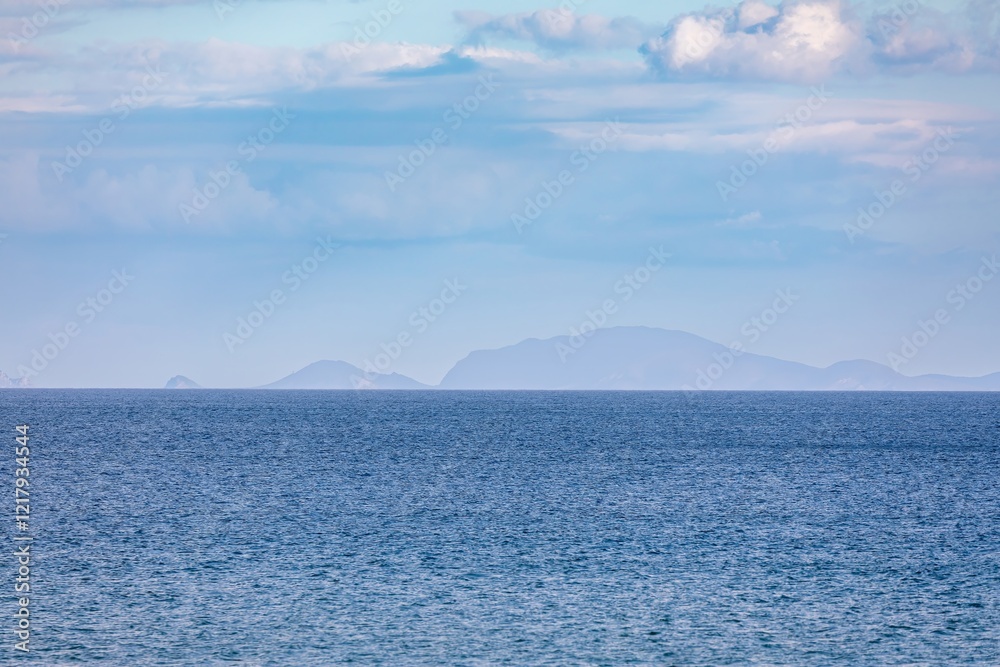 Calm ocean waves meet a hazy mountain range. Vastness of nature. Matauri Bay, Matauri Bay, Northland, NZ Calm ocean waves meet a hazy mountain range. Vastness of nature. Matauri Bay, Matauri Bay, Northland, NZ