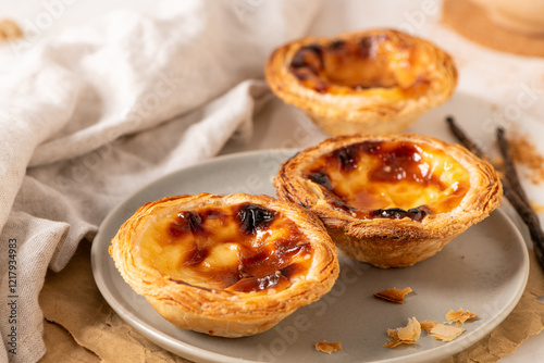 Fototapeta Naklejka Na Ścianę i Meble -  Three Pastel de Nata, Portuguese custard tarts, are presented on a plate with cinnamon and vanilla beans.