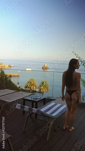 Vertical view of a woman relaxing on a lounge chair near an infinity pool with a stunning ocean view at sunset. Slow motion lifestyle vacation video in Madeira