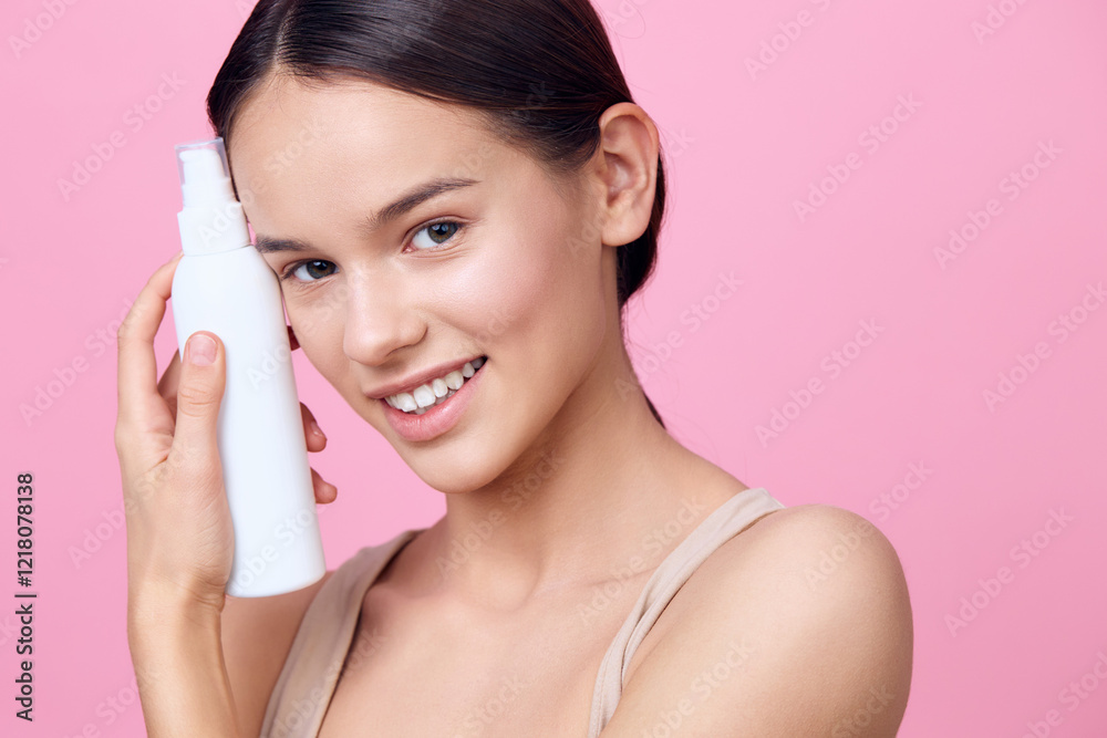 Young woman with clear skin holding a skincare bottle on a pink background, promoting beauty and self care products, showcasing radiant beauty and confidence Young woman with clear skin holding a skincare bottle on a pink background, promoting beauty and self care products, showcasing radiant beauty and confidence