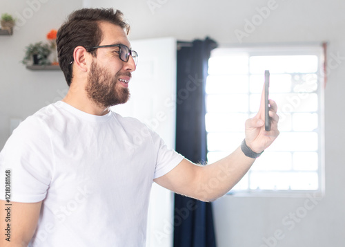 Joven apuesto de barba teniendo una videollamada con sus empleados. Hombre con anteojos dando indicaciones desde su teléfono celular 