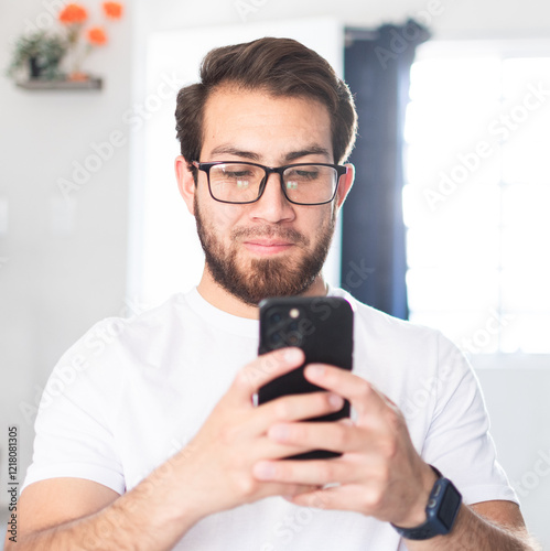Joven de buen ver, escribiendo un mensaje en su teléfono celular. 