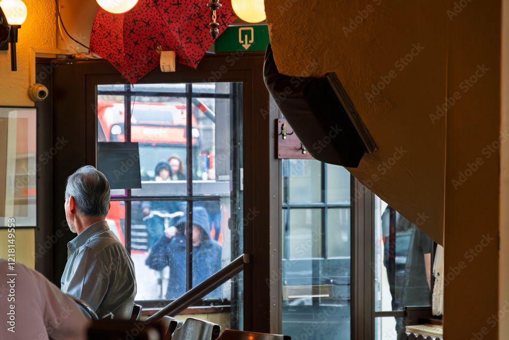Bar patrons stay warm inside an English pub while outside buses and pedestrians walk in the rain on a winter day. Bar patrons stay warm inside an English pub while outside buses and pedestrians walk in the rain on a winter day.