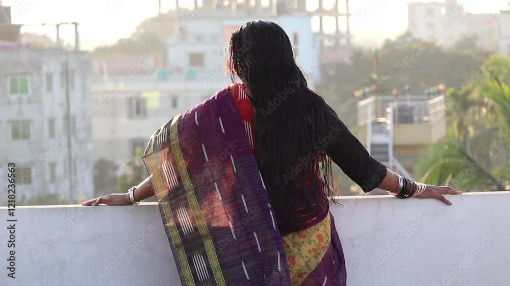 A Bengali woman in a beautiful cotton saree stands on the rooftop, enjoying an afternoon alone. Back view.
