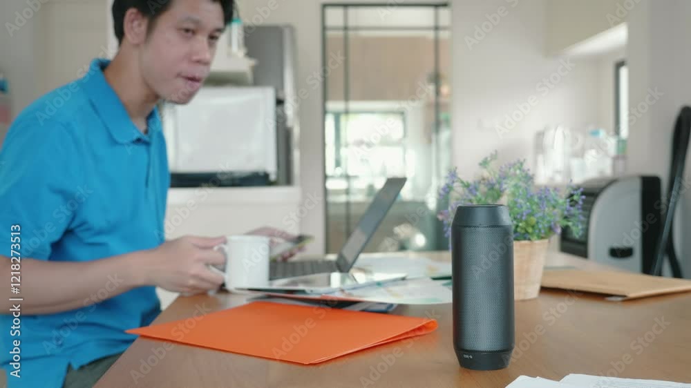 A man is sitting at a table with a laptop and a smart speaker. Scene is focused and serious, as the man is working on something important A man is sitting at a table with a laptop and a smart speaker. Scene is focused and serious, as the man is working on something important