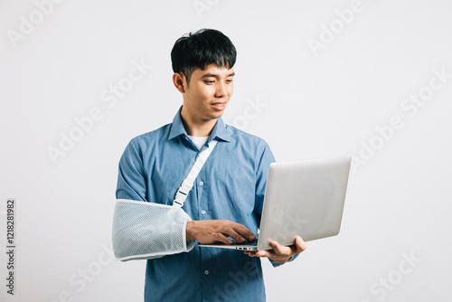 A resilient Asian businessman, with a broken arm in plaster, remains committed to work, holding a laptop. Studio shot isolated on white, emphasizing dedication and recovery. photo