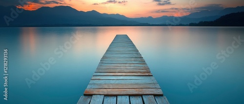 Serene wooden pier extending into calm waters at sunset, surrounded by mountains and soft clouds photo