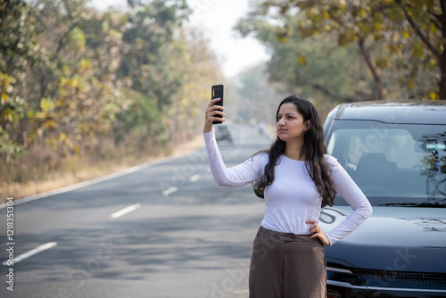 Young woman searching for a mobile network in the forest with her damaged car, bad connection and no signal concept image