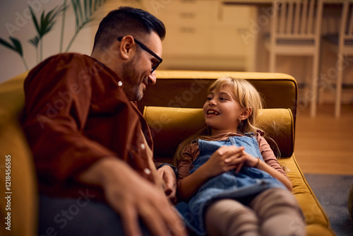 Happy little girl and her father communicating while relaxing on sofa.