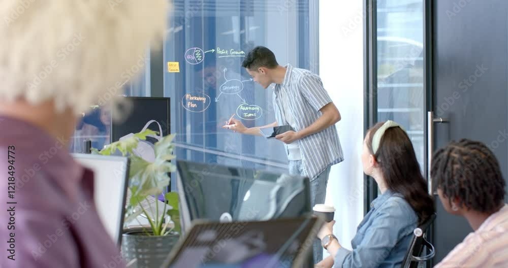 Presenting marketing plan, man writing on glass board in office meeting