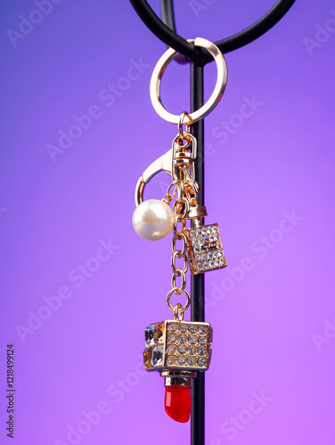 close up of cute bright red lipstick keychain with white rhinestone case on purple background photo