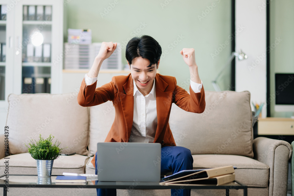 Obraz premium Asian entrepreneur focused on work, analyzing documents with a laptop on sofa in a stylish office.