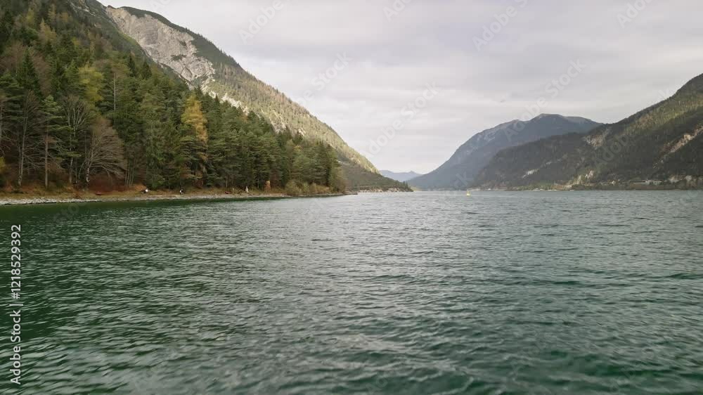 A serene drone shot at Achensee, hovering over the waters while moving backward. The tranquil lake and stunning alpine surroundings create a breathtaking scene. A serene drone shot at Achensee, hovering over the waters while moving backward. The tranquil lake and stunning alpine surroundings create a breathtaking scene.
