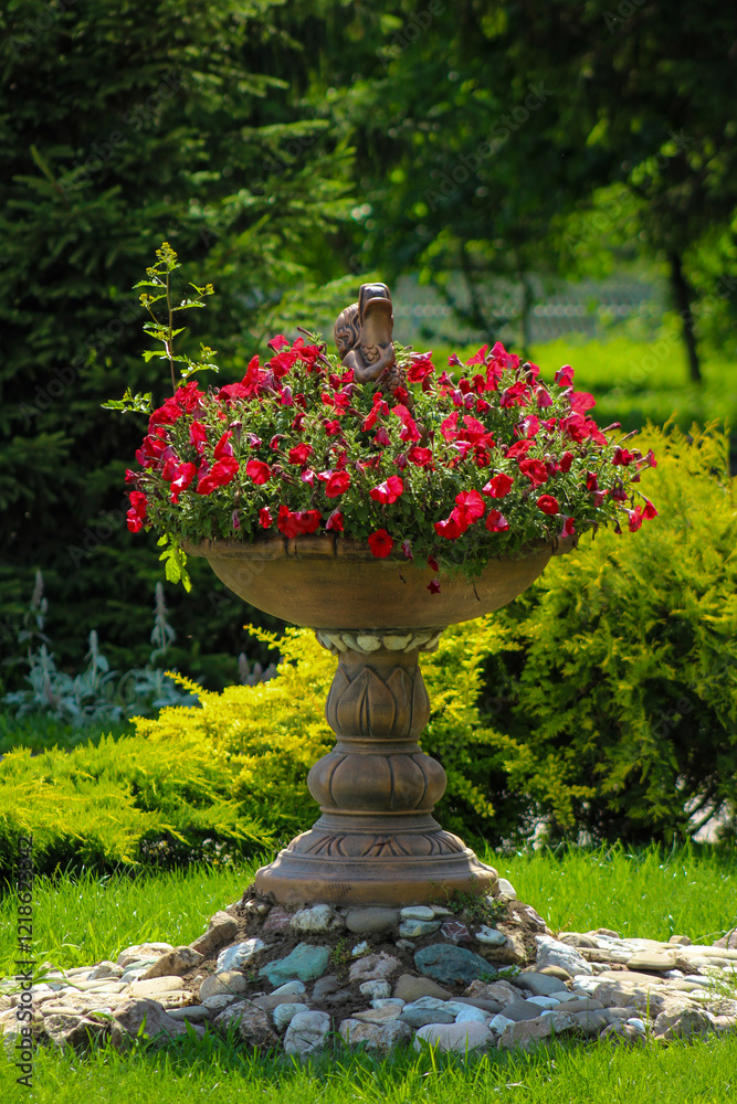 A flower pot with red flowers in the middle of a garden A flower pot with red flowers in the middle of a garden