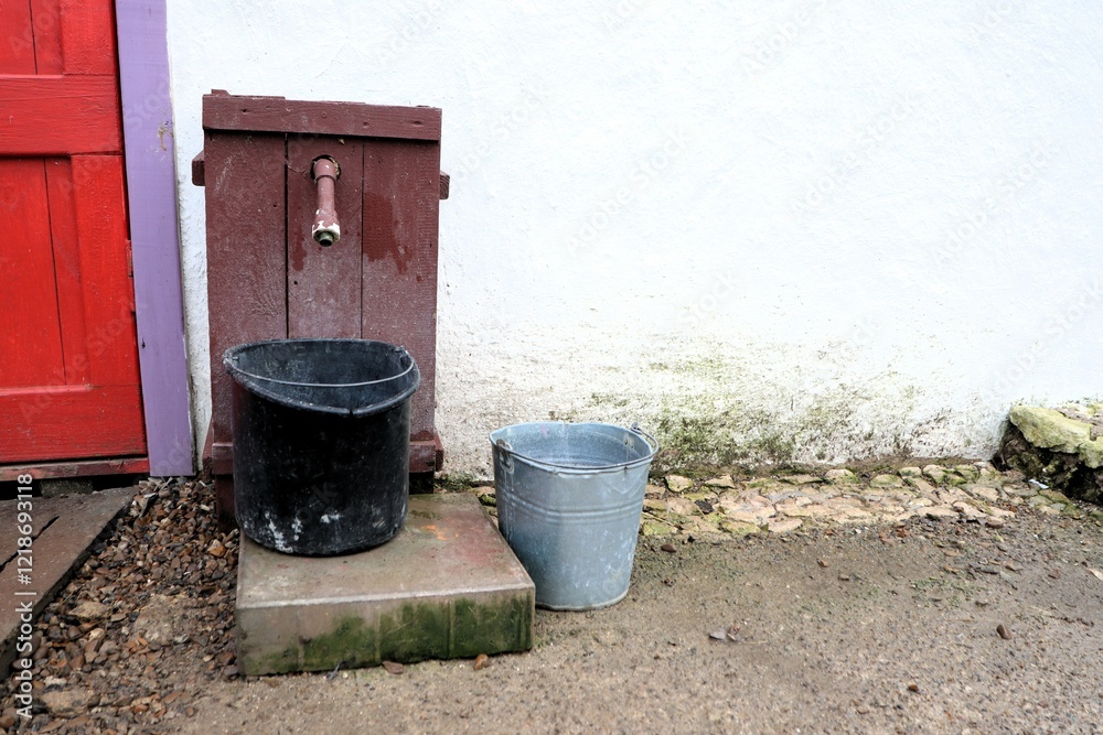 A water source with charming buckets by a lovely red door that enhances the scenery A water source with charming buckets by a lovely red door that enhances the scenery