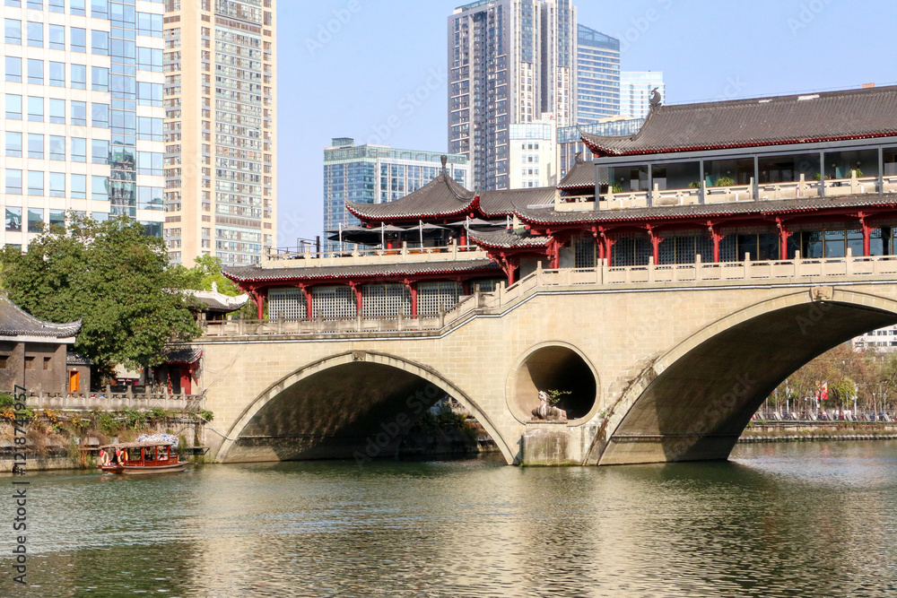 Obraz premium Landscape shot as little Chinese wooden boat heads towards the archway of the iconic ancient Anshun Bridge on the Jinjiang River of Chengdu, mega city in China known for its relaxed lifestyle