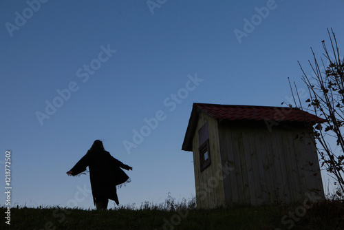 Silhouetted Figure in a Mysterious Twilight Scene Near a Small Wooden Cabin