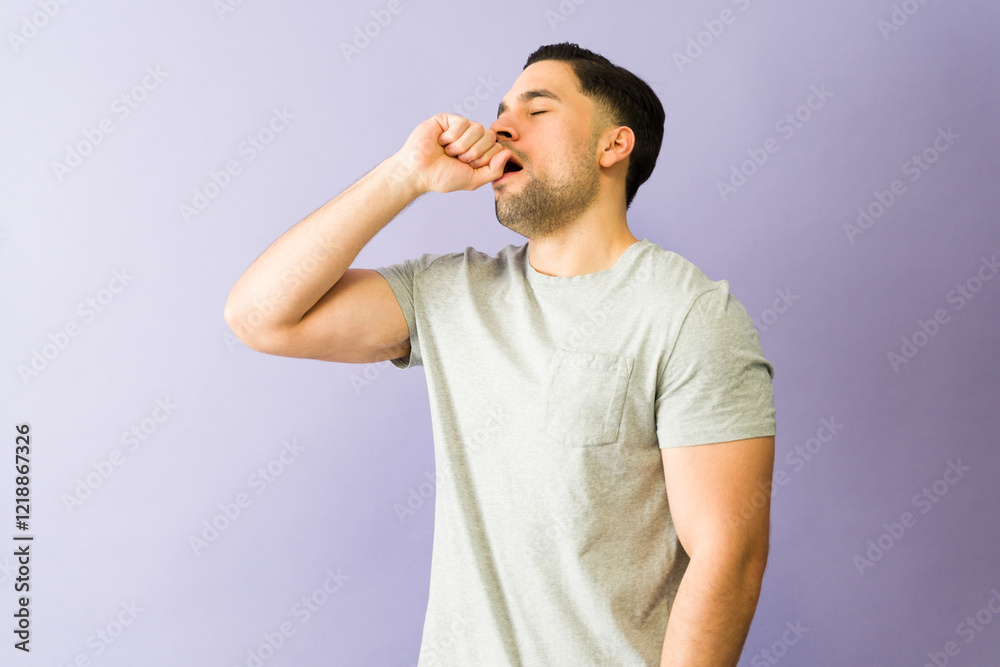 Young man yawning and covering mouth with hand on purple background Young man yawning and covering mouth with hand on purple background