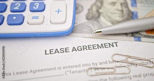 Lease agreement documentation and financial planning. A lease agreement, a calculator, pen, and paper clips, emphasizing financial calculations and legal preparations for rental or leasing contracts.