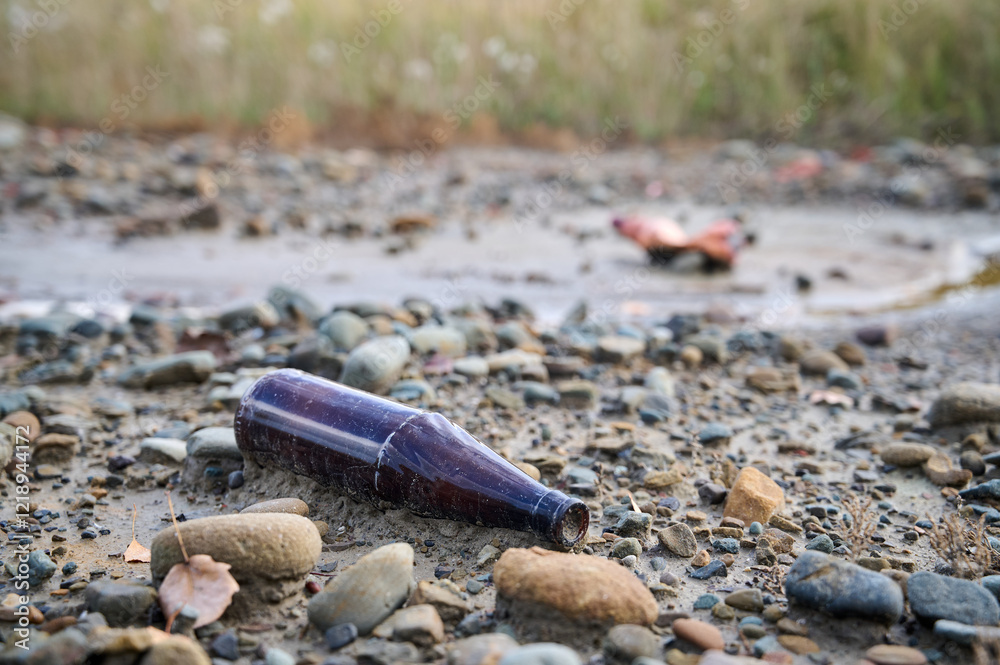 Discarded glass bottle among pebbles in a natural setting near a riverbank at sunset Discarded glass bottle among pebbles in a natural setting near a riverbank at sunset
