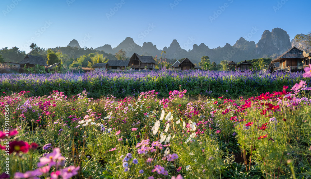 Obraz premium A vibrant landscape filled with colorful flowers, rolling hills, and quaint huts under a clear blue sky.