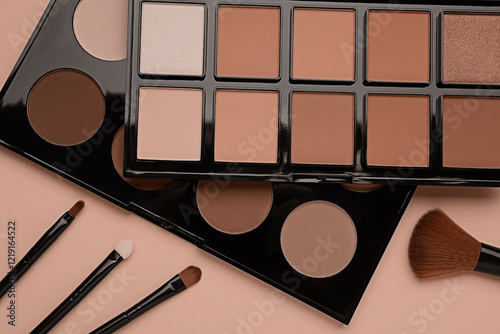 Eyeshadow palettes in mocha mousse shades and makeup brushes on dark beige background, top view. Trendy color of 2025 year photo