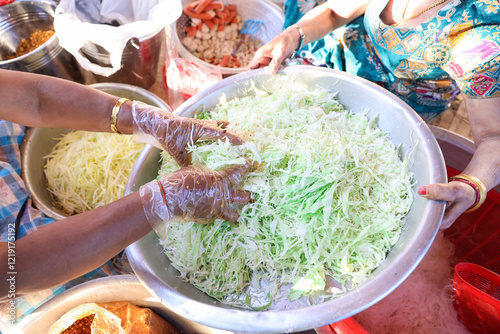 The woman's hand is picking up cabbage,  for salad thinly shredding it, and placing it in a large stainless steel bowl with vegetables and other condiments around it, looking beautiful. photo