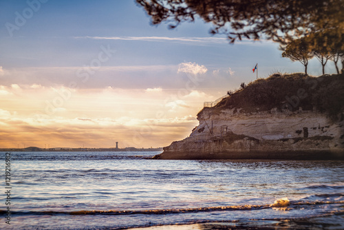 Paysage côtier serein capturé au coucher du soleil, mettant en avant une falaise surplombant l'océan avec une cabane de pêche traditionnelle et un drapeau flottant. photo