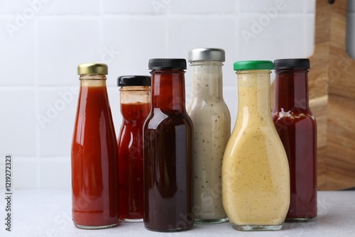 Tasty sauces in glass bottles on white table, closeup photo