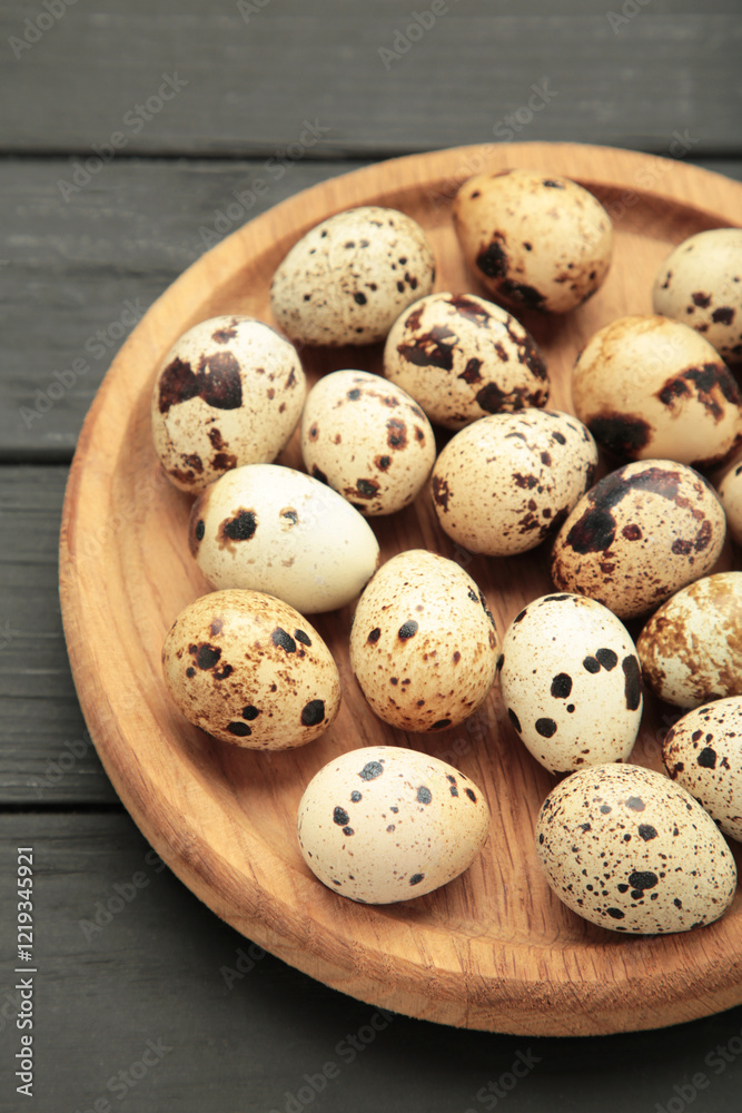 Quail eggs in wooden plate on black wooden background. Vertical photo. Quail eggs in wooden plate on black wooden background. Vertical photo.