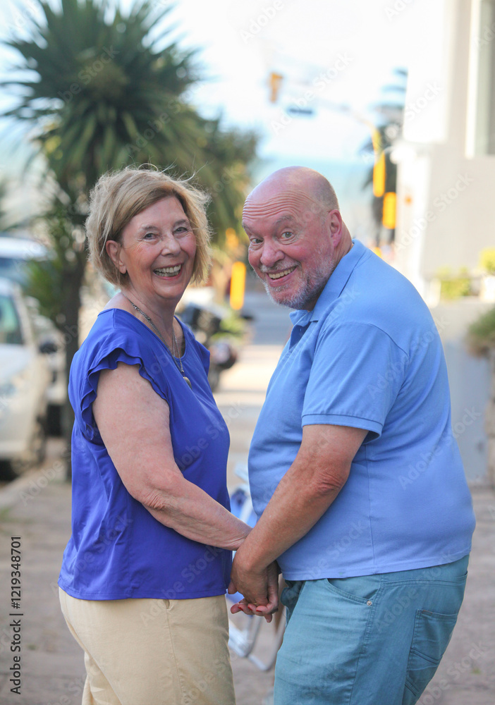 Naklejka premium happy senior couple smiling walking down the street holding hands on summer day