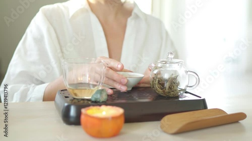 Female enjoying aged white tea taste and aroma from porcelain teacup exuding warmth and tranquility. Elegant setup with teapot and glass pitcher enhances an intimate, soothing tea ceremony experience photo