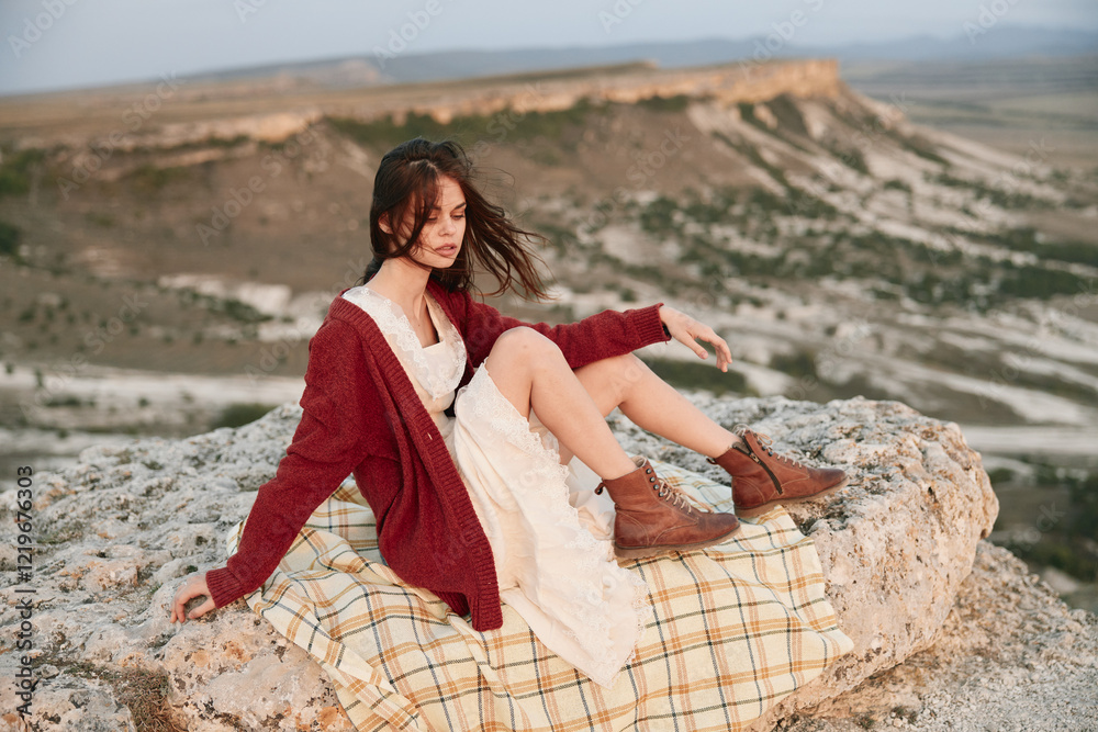 Woman sitting atop mountain in red sweater and brown booties enjoying scenic beauty of nature Woman sitting atop mountain in red sweater and brown booties enjoying scenic beauty of nature