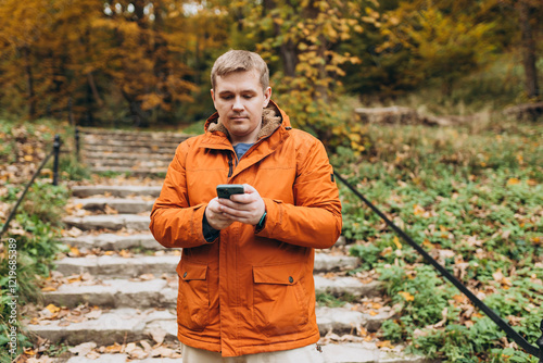 Obraz na płótnie Adult 30s man hiker stand outdoors in a natural setting, smile while using his mobile phone outdoors. Hiking, lifestyle, adventure and tourism concept. w salonie