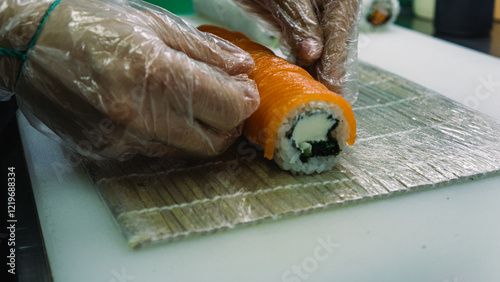 The chef places slices of salmon on a rice roll. Inside is cream cheese. Preparing a Philadelphia roll. Delivery-only restaurant. Close up. photo