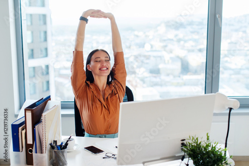 Happy lady manager sitting on chair and stretching her back and arms, taking break, feeling pleased and satisfied at workplace in office